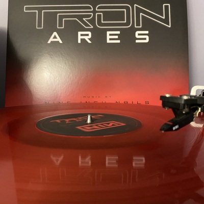 photograph of tron: ares soundtrack vinyl playing, with the packaging in the background