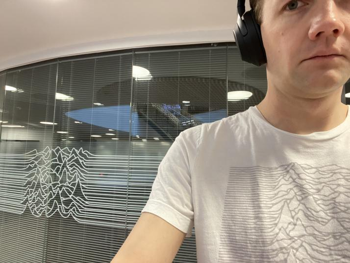 photo of me wearing an Unknown Pleasures t-shirt alongside a meeting room decal of the same