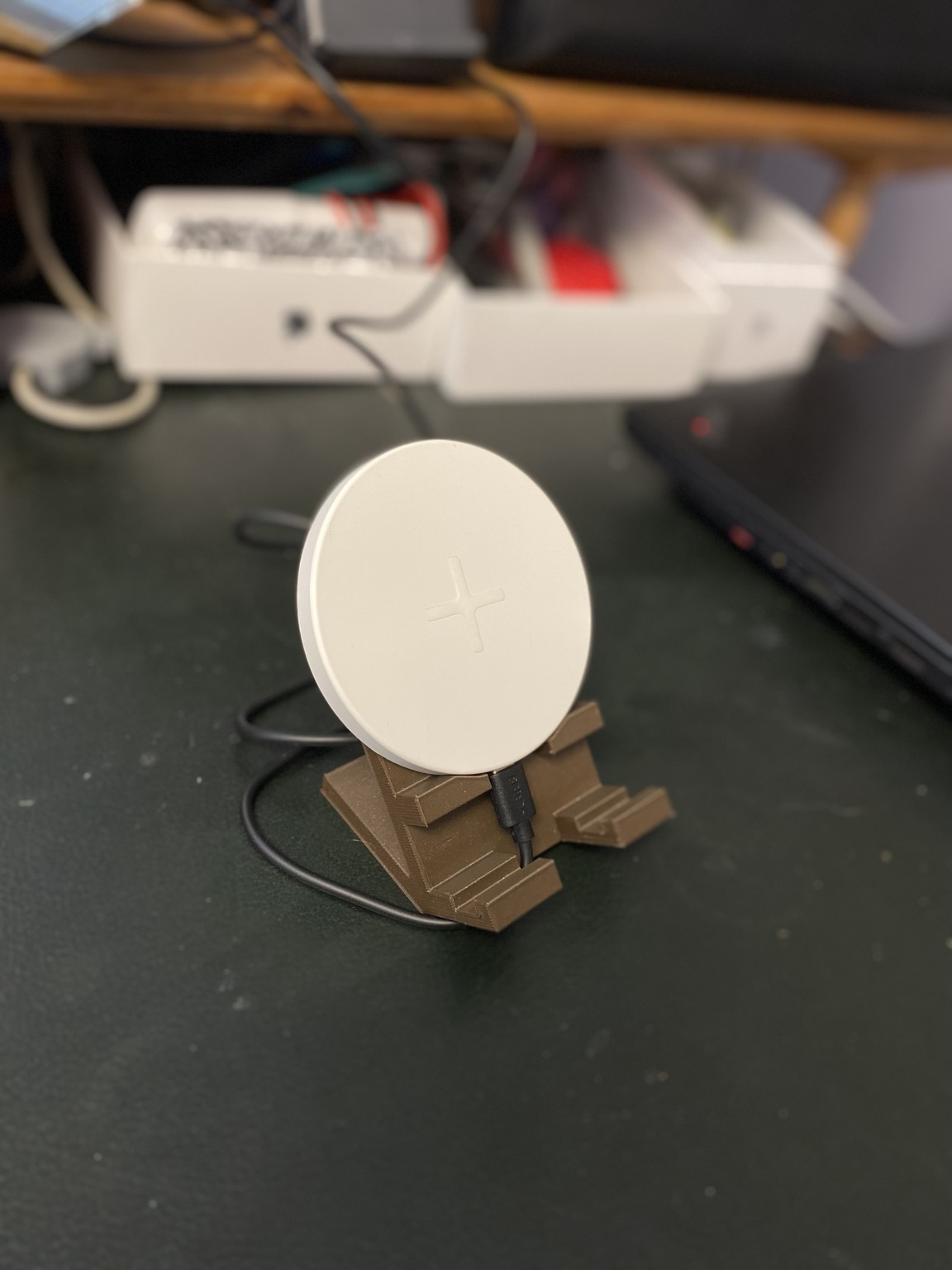 Puck shaped qi charger sitting on stand which orients it forward about 45°