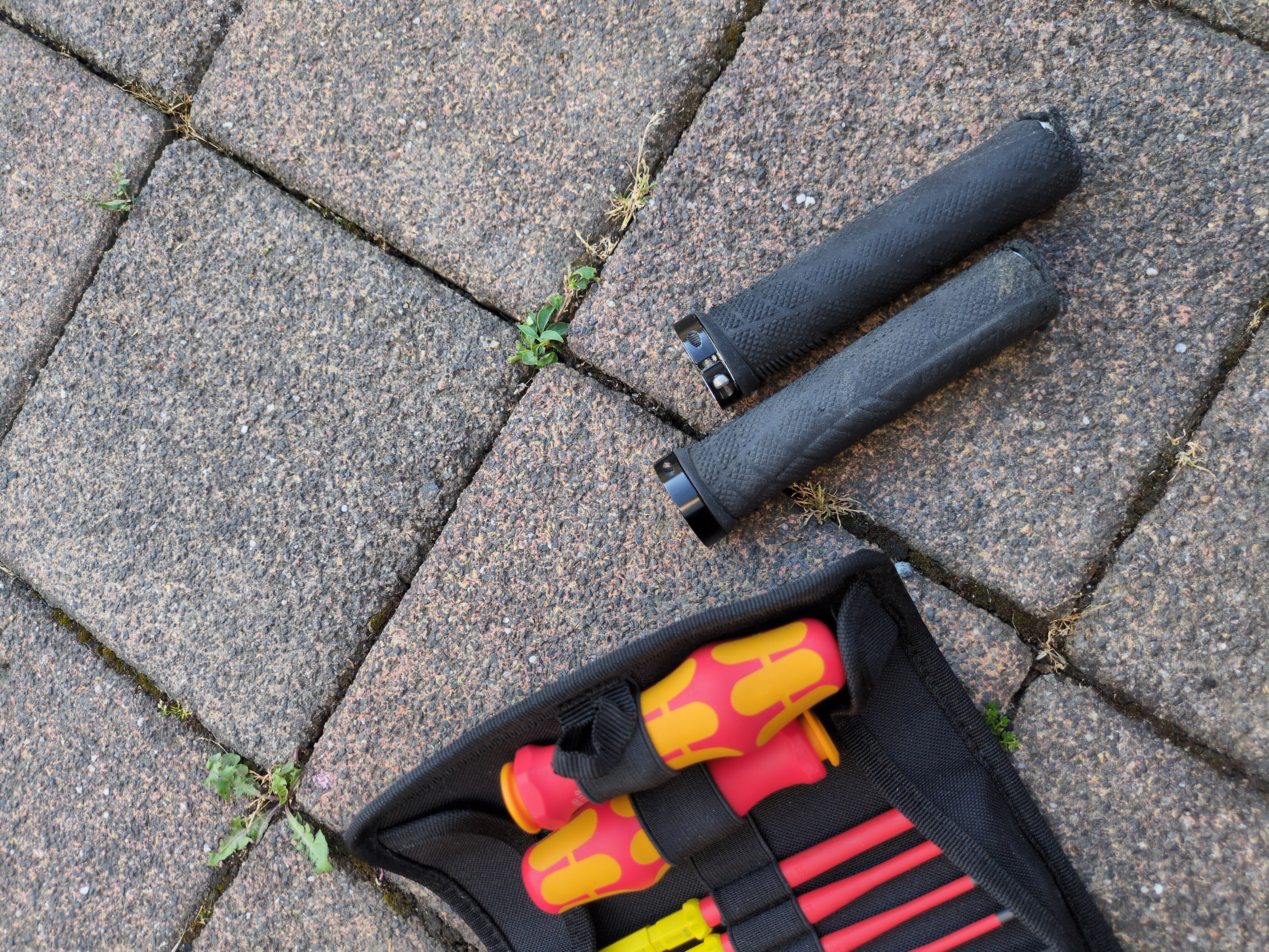 Two old, worn bikehandles on the ground , a screwdriver tool set beside it
