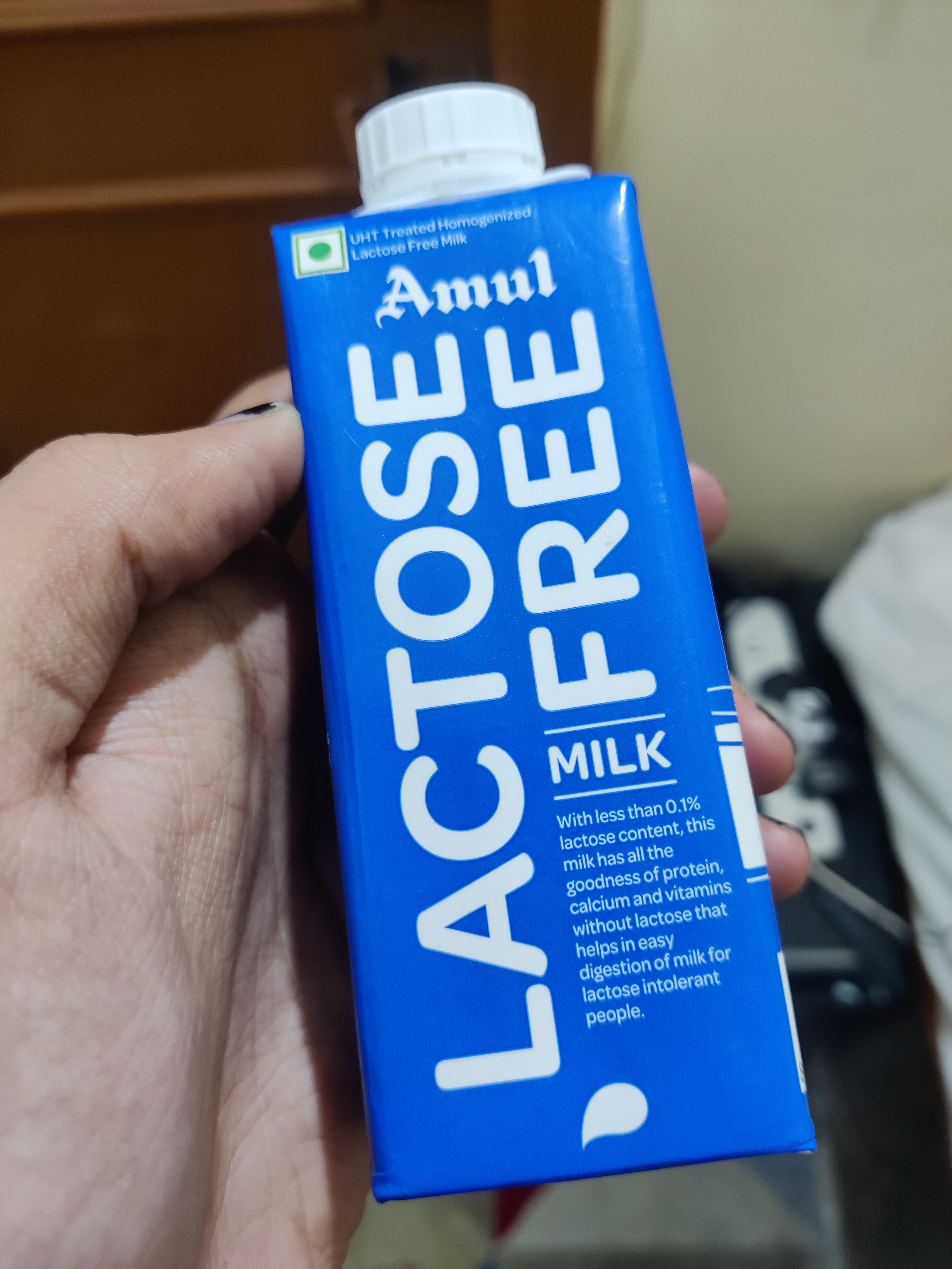 Hand holding a 250ml tetrapack carton in blue reading "Lactose Free Milk" on it