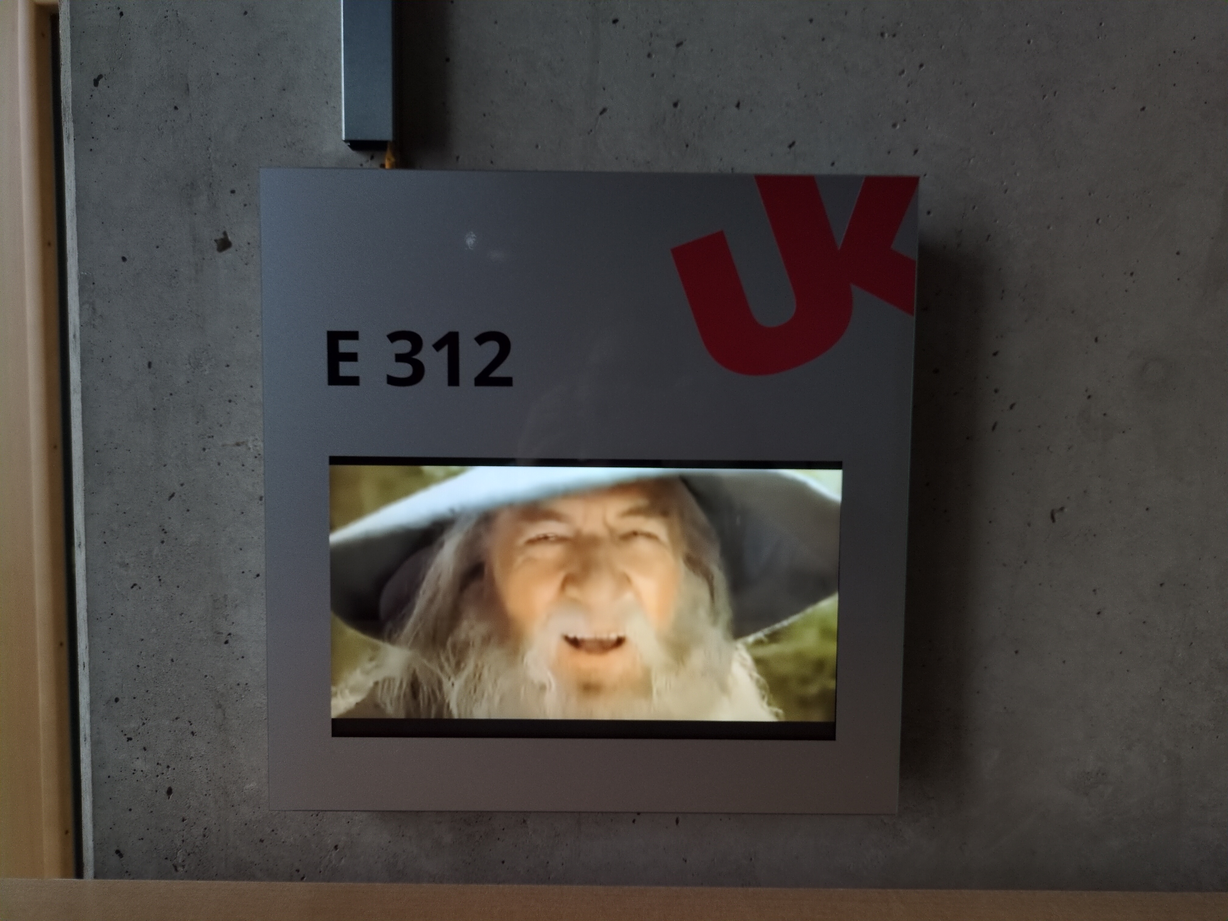 A uni Koblenz room sign that is hacked to display a laughing Gandalf 