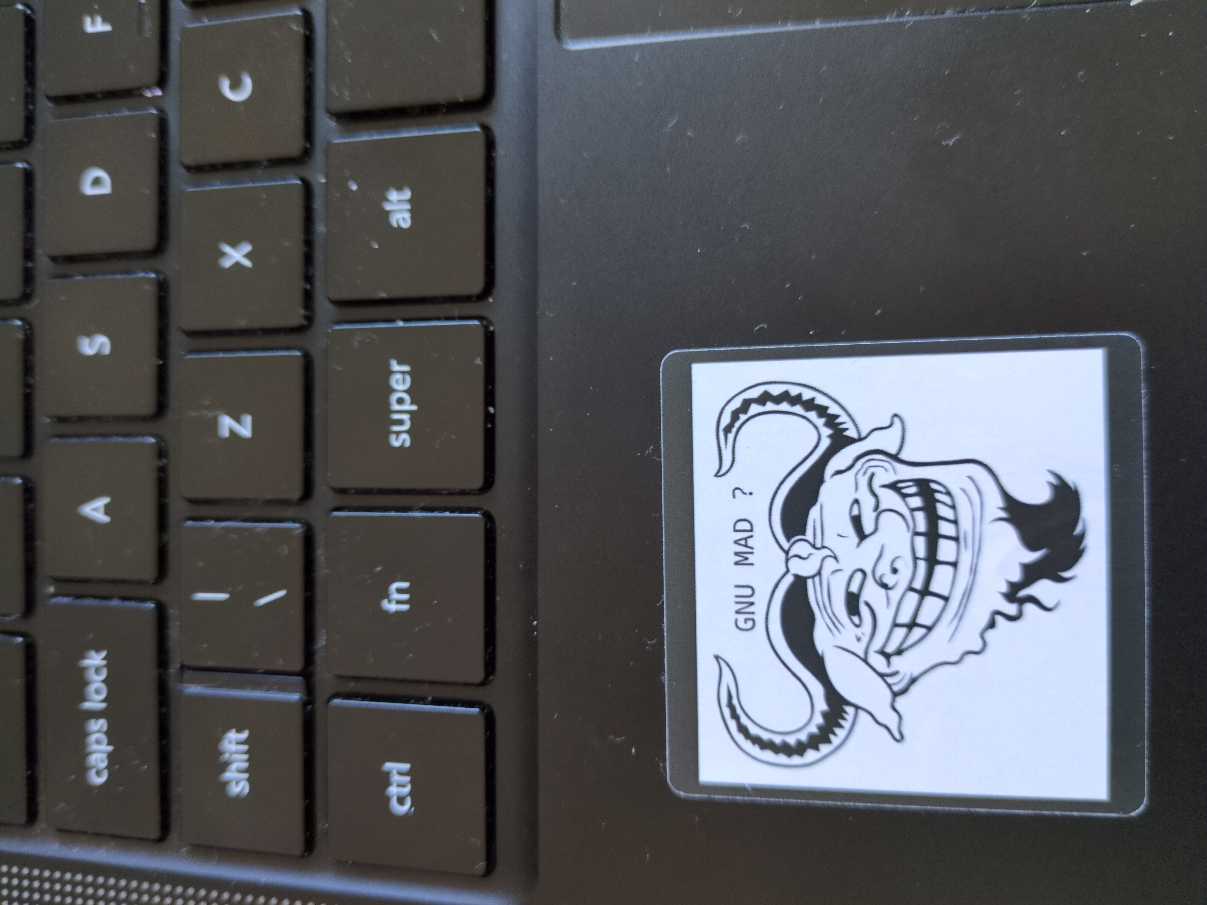 A sticker on a black laptop showing a crossover between the trollface and the GNU logo titled "GNU MAD?" 